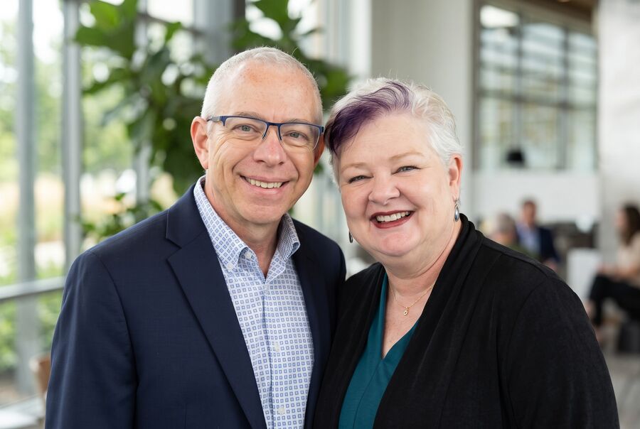 Close-cropped portrait of Brian and Robin Joy Olson leaning together, laughing, with lobby greenery behind them.
