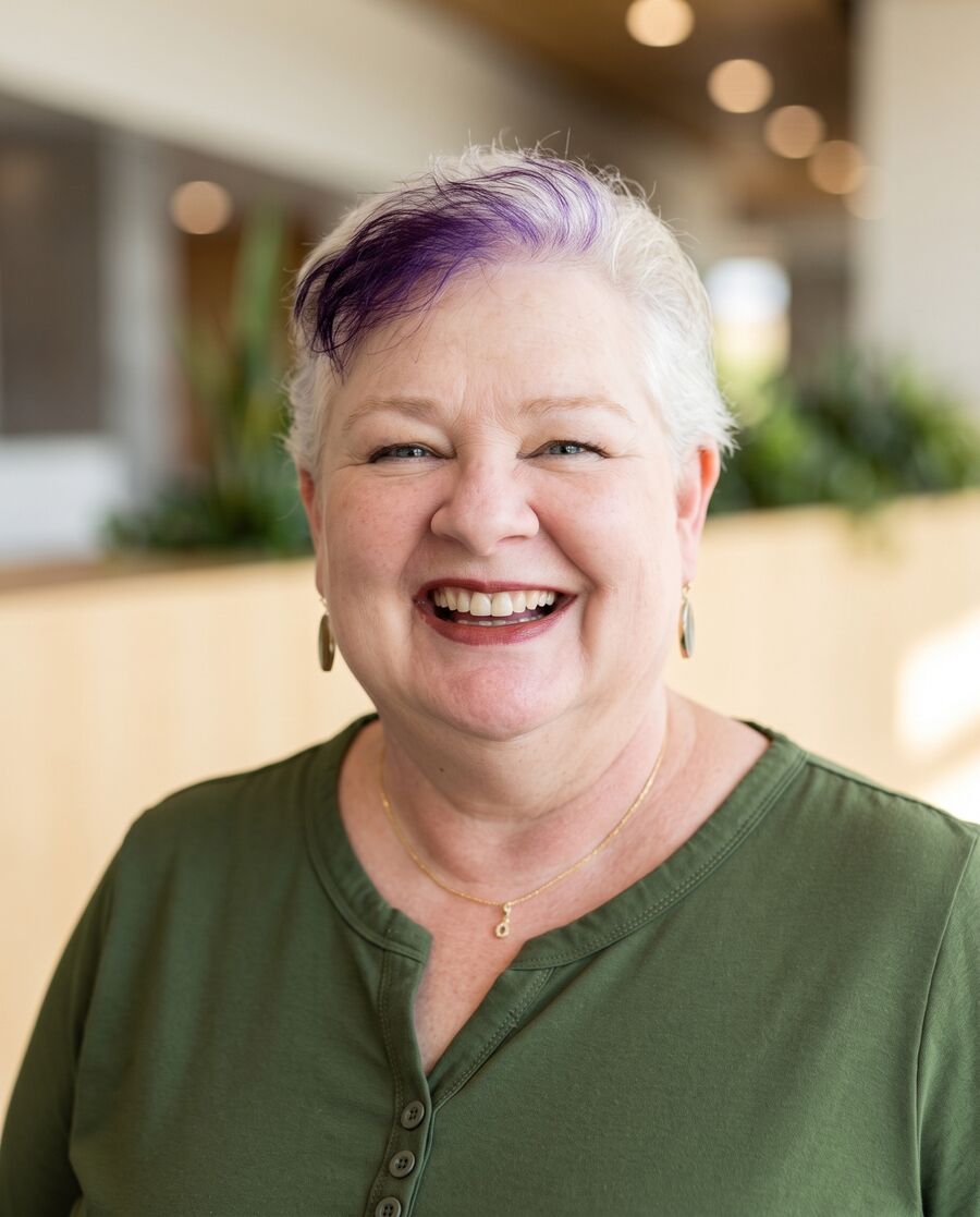 Robin Joy Olson laughing in a lobby, plants and warm ceiling light behind her.